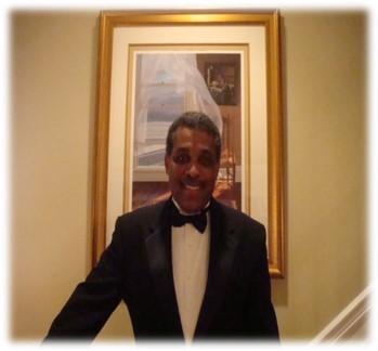 Man in tuxedo standing before framed artwork.